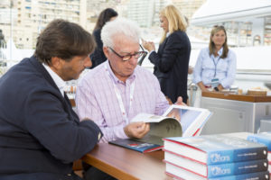 Lamberto Tacoli CEO Perini Navi with author, and yacht designer Ron Holland at Monaco Yacht Show 2018, ready to sign copies for guests at reception held aboard Perseus^3 a 60 metre sailing yacht, that is a Ron Holland - Perini Navi collaboration