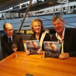 Simon and Patricia Groom with Paul Archer show off their copies of All The Oceans, yacht designer Ron Holland's memoir at Monaco Yacht Show reception 2018
