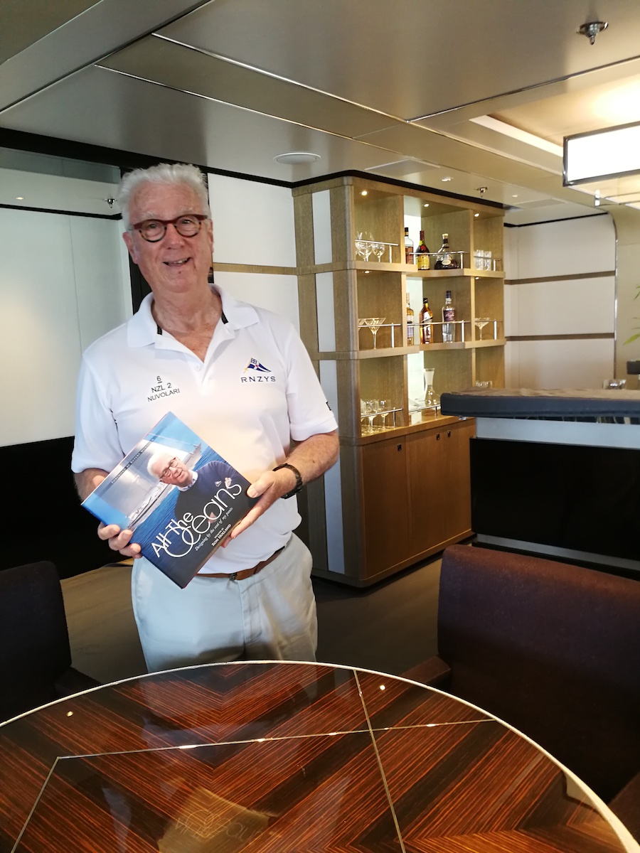 Ron Holland aboard sailing yacht M5 with a copy of his book All The Oceans